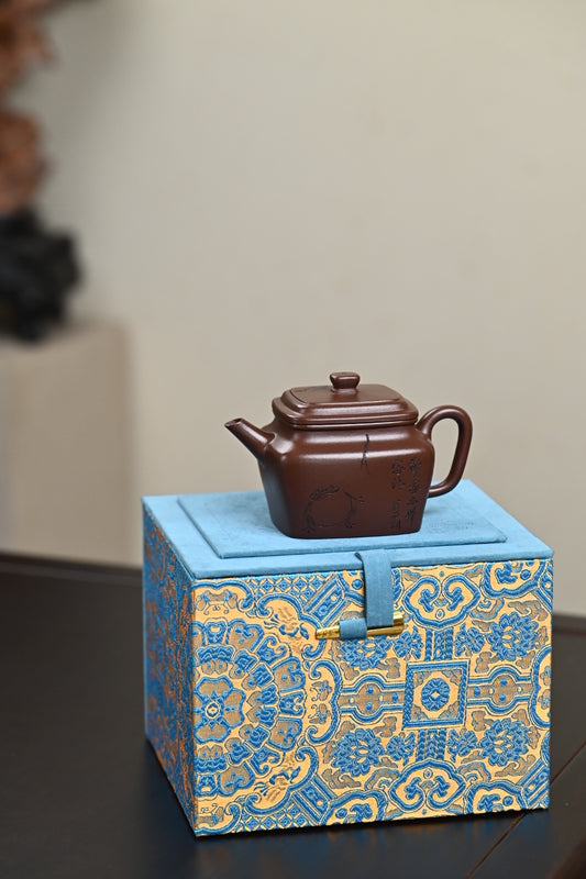 Handmade Yixing purple sand teapot displayed on a decorative blue and gold box.