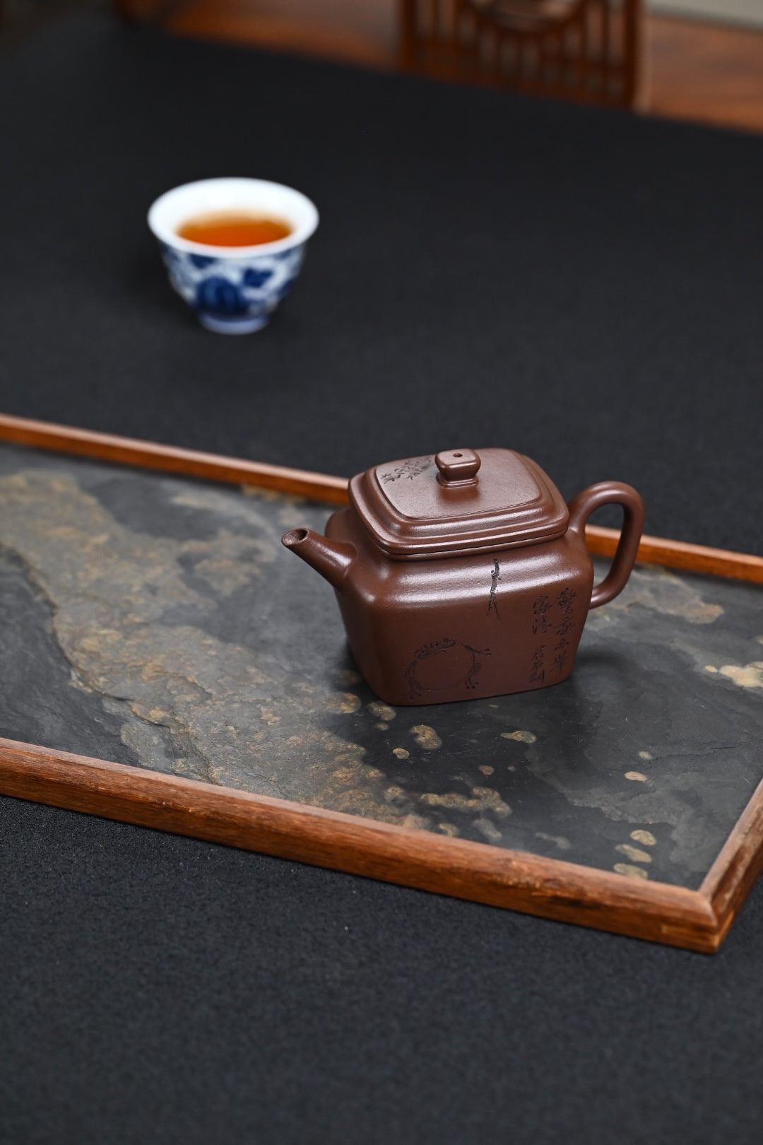 Handmade Yixing purple sand teapot on a wooden tray with tea cup in the background, showcasing traditional Chinese craftsmanship.