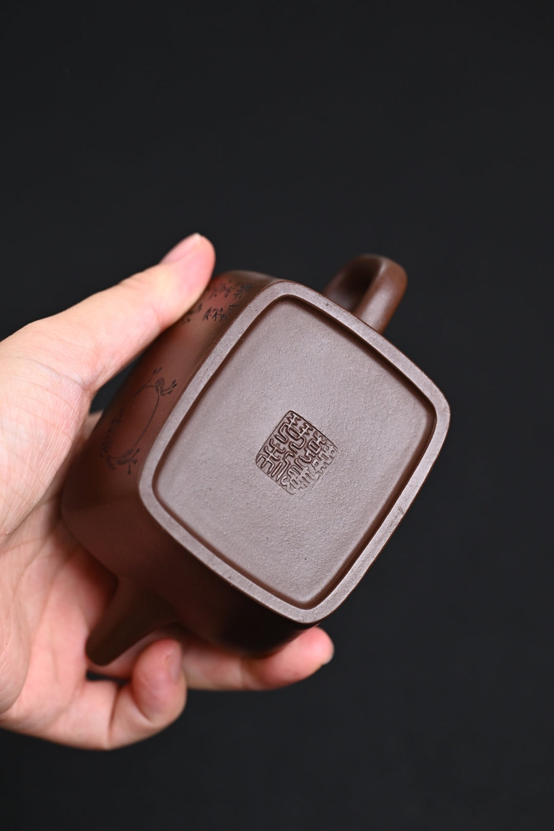 Handmade Yixing purple sand teapot showcasing the base design and craftsmanship, held in a hand.