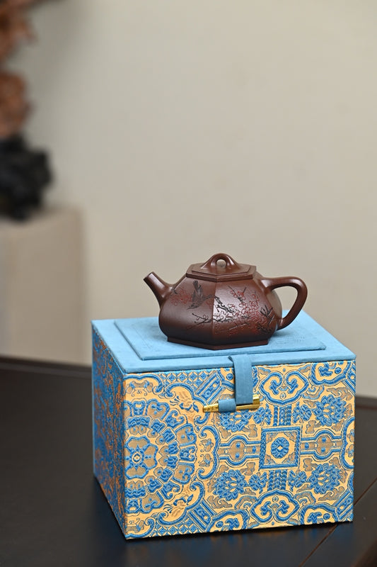 Handmade Yixing purple sand teapot displayed on an ornate blue and gold gift box.