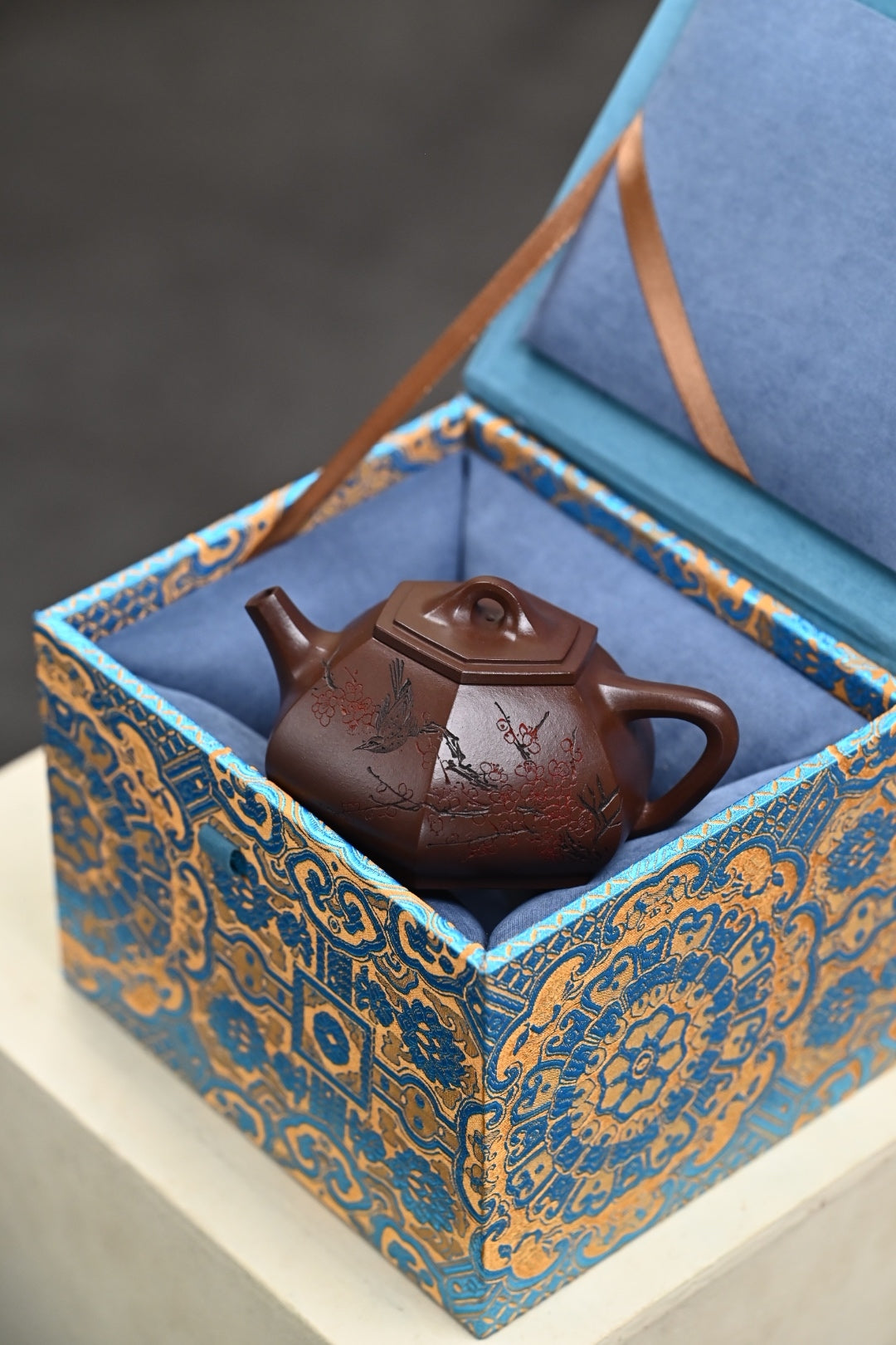 Handmade Yixing purple sand teapot in an ornate blue and gold gift box, highlighting craftsmanship and elegance.