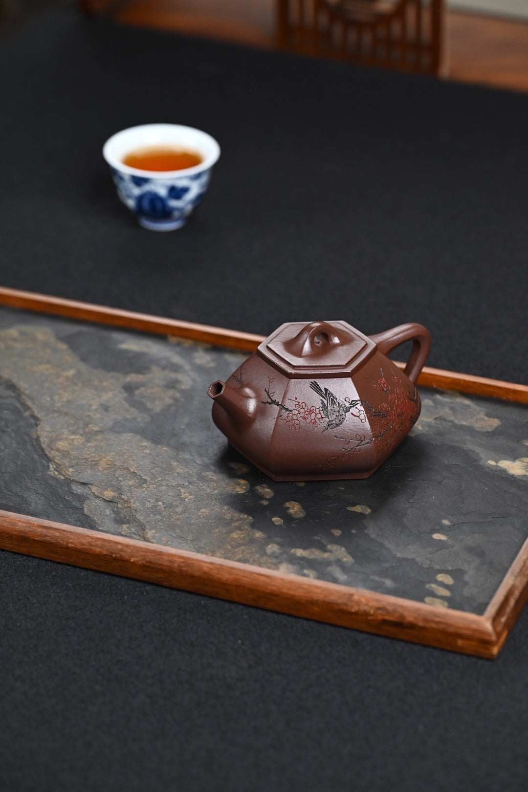 Handmade Yixing purple sand teapot on a serving tray with a tea cup in the background.
