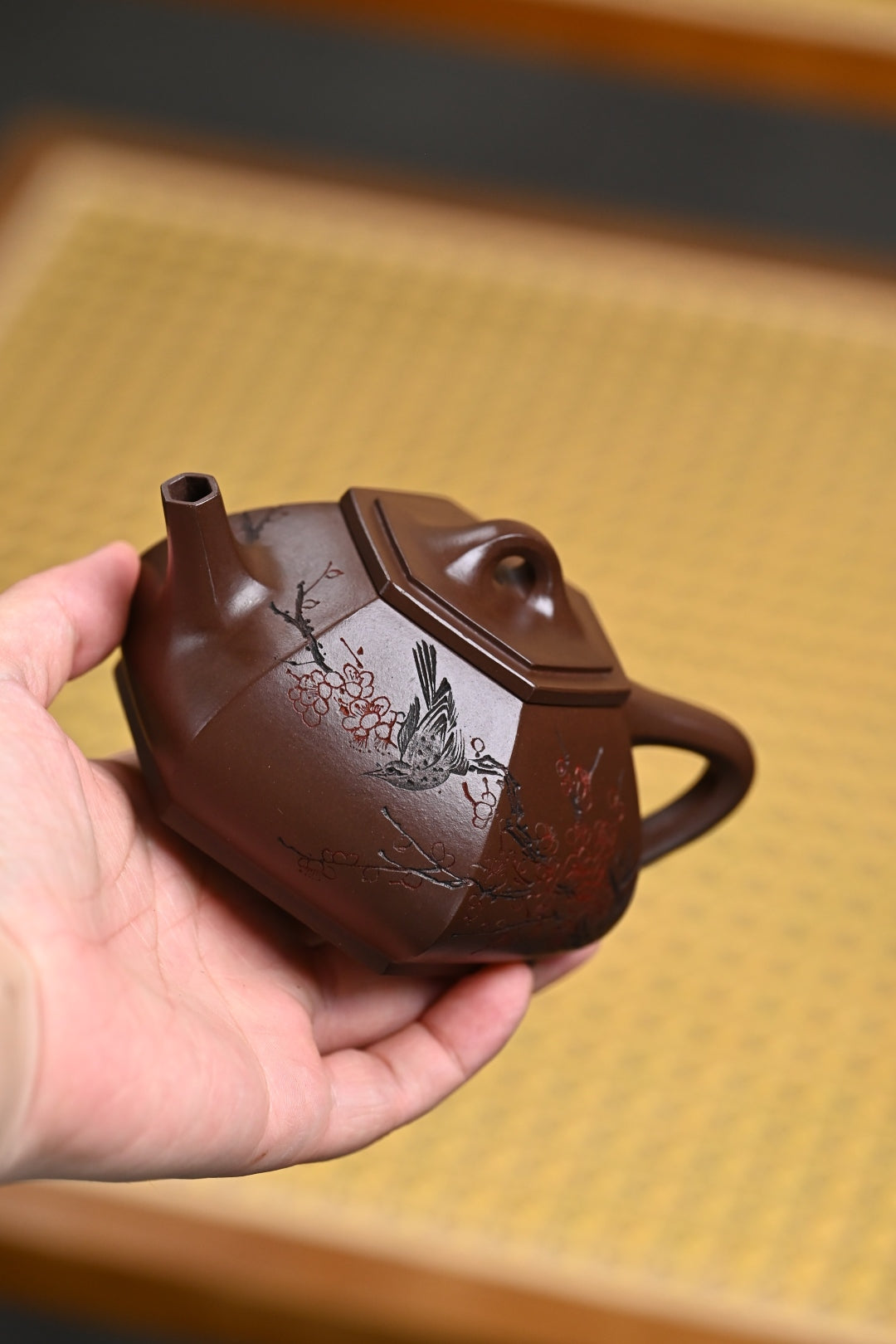 Handmade Yixing purple sand teapot held in hand, featuring exquisite craftsmanship and detailed artwork.