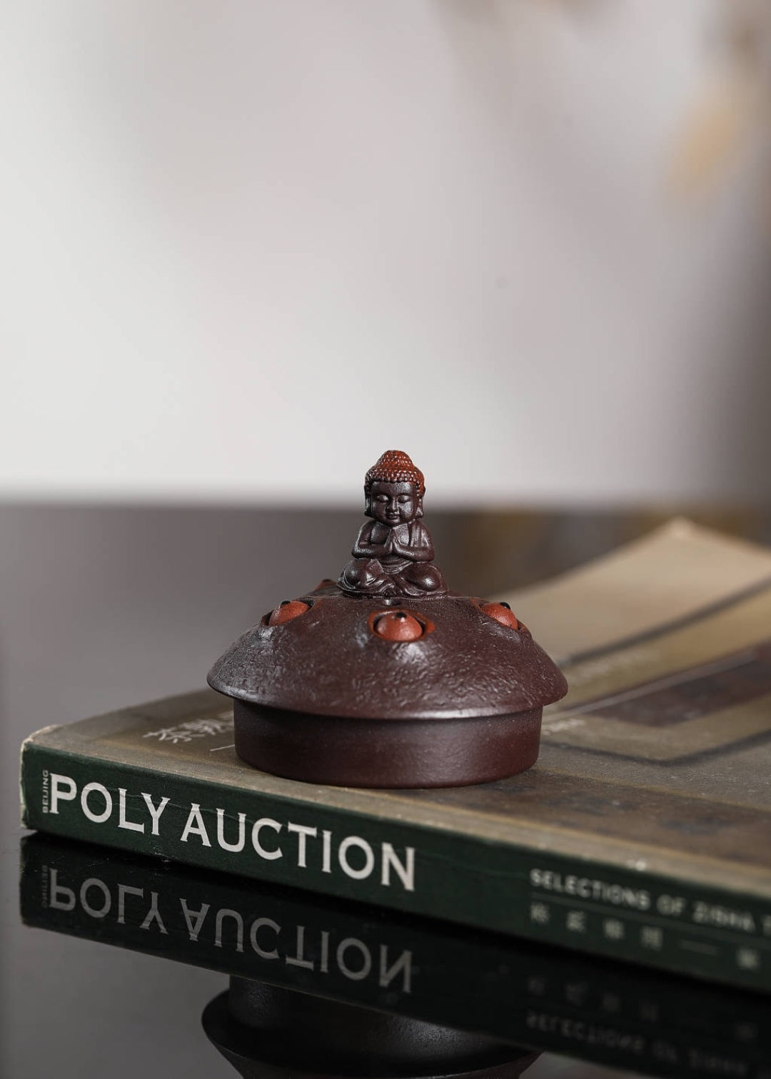 Handmade Yixing purple sand teapot with intricate design and Buddha figurine, displayed on a book.