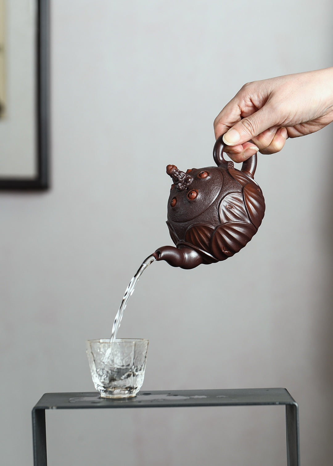 Handmade Yixing purple sand teapot pouring water into a glass cup, showcasing detailed craftsmanship.