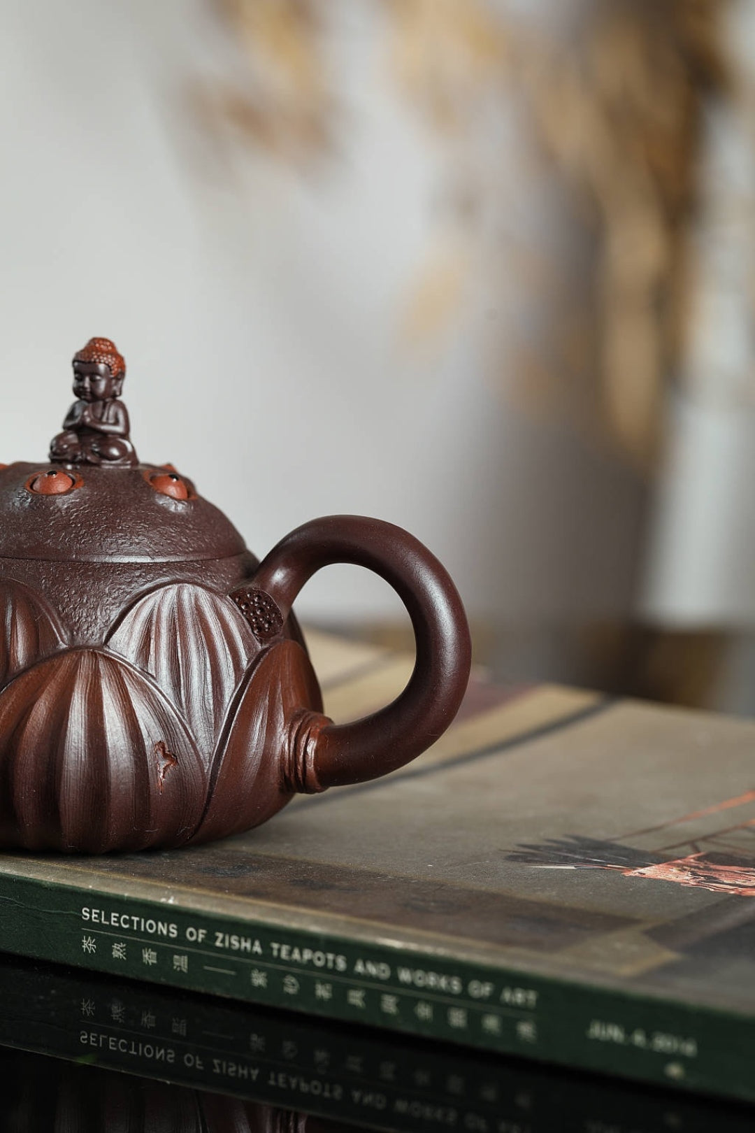 Handmade Yixing purple sand teapot with lotus design, showcasing intricate craftsmanship on a book.