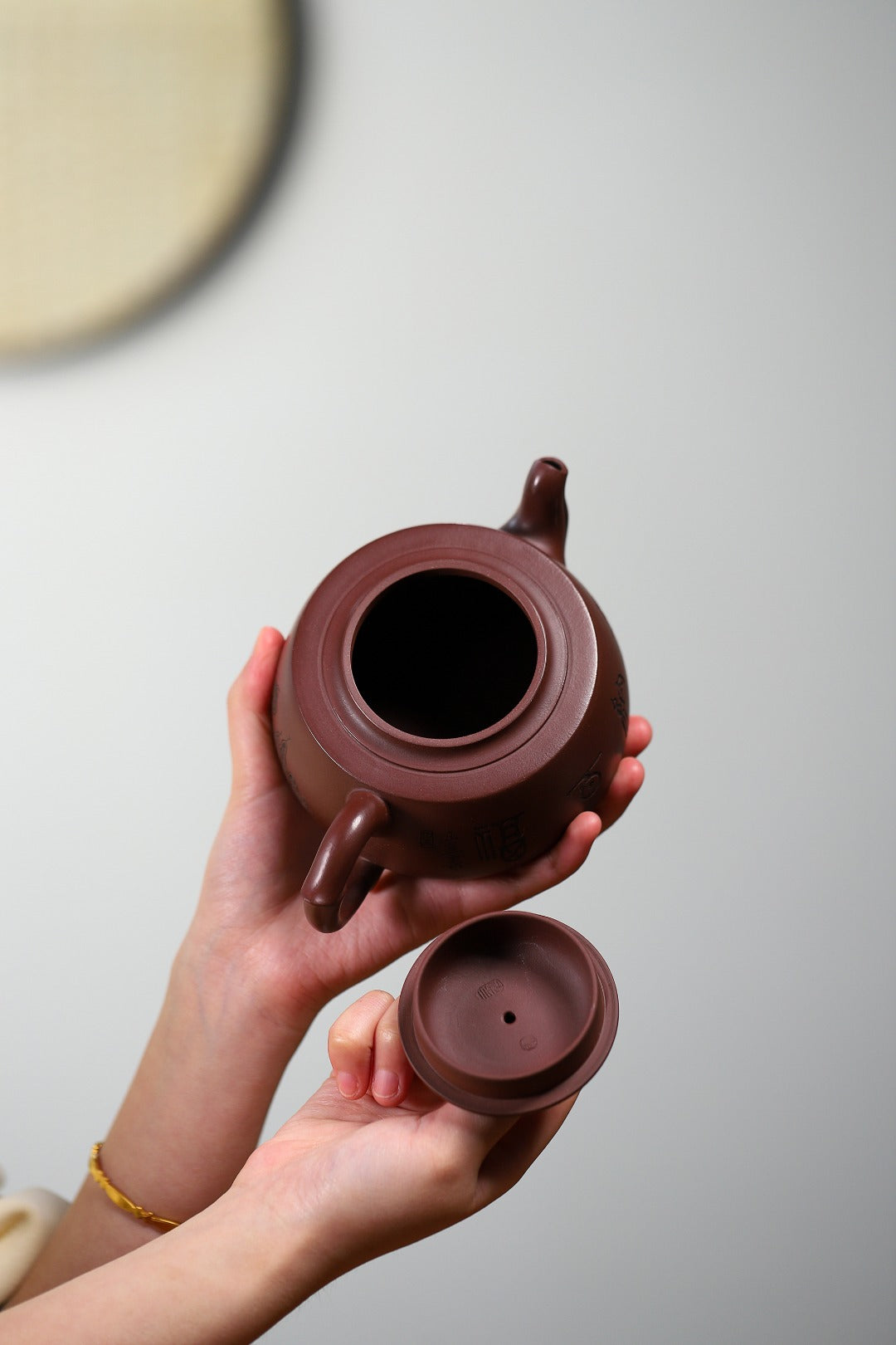 Handmade Yixing purple sand teapot held by hands, showcasing the lid and unique design.