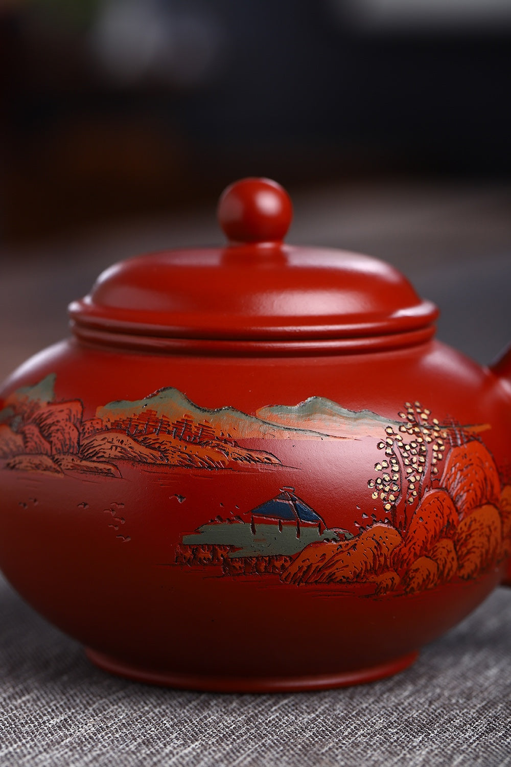Handmade Yixing purple sand teapot with vibrant red glaze and landscape painting design, showcasing artisanal craftsmanship.