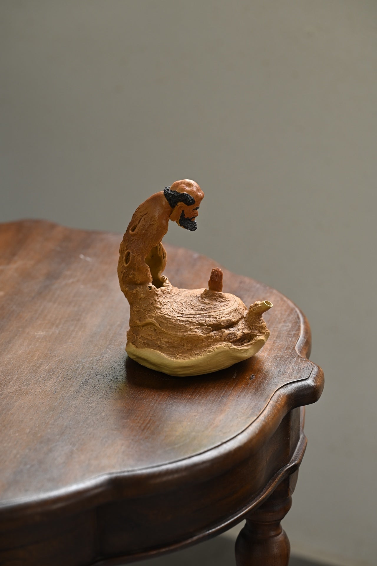 Handmade Yixing purple sand teapot sculpted to resemble a meditating figure on a wooden table.