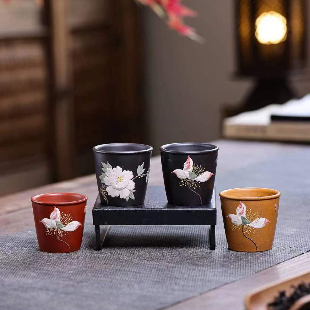 Handmade Yixing Zisha cups crafted from original purple sand by skilled artisans, featuring floral designs and warm colors.