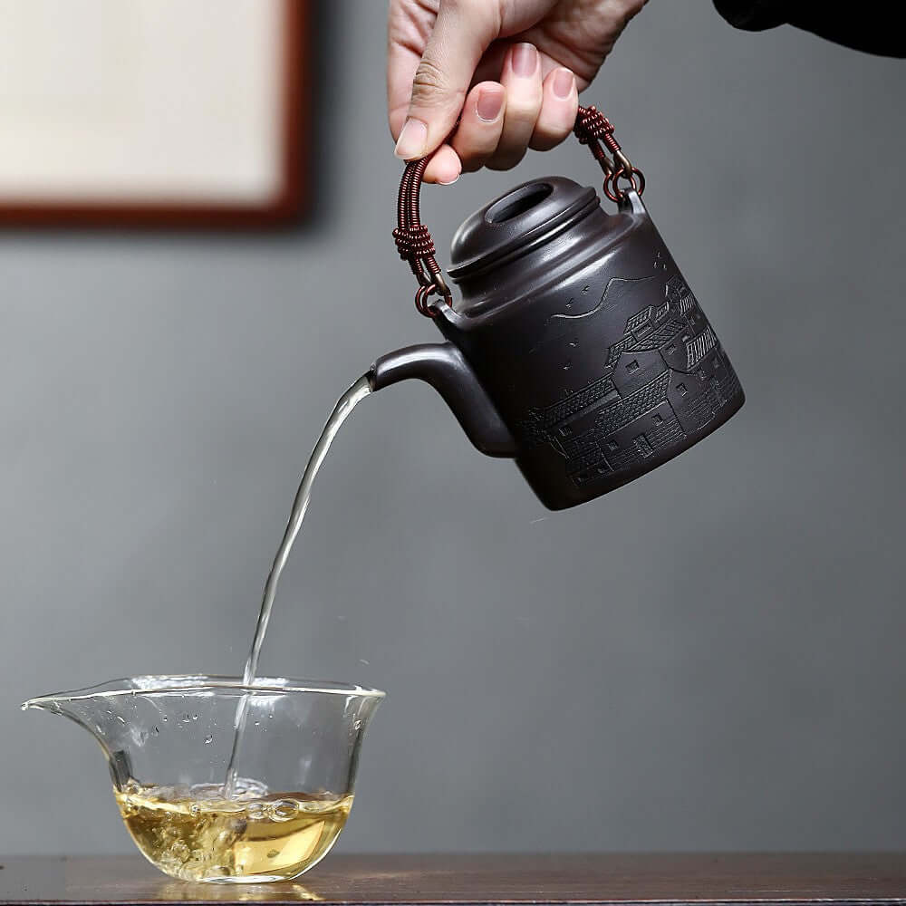 Handmade Yixing purple sand teapot pouring tea into a glass cup, showcasing traditional craftsmanship.