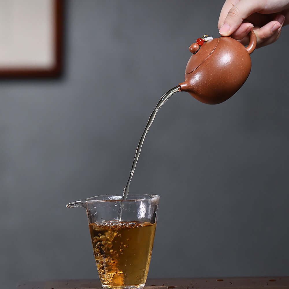 Handmade Yixing purple sand teapot pouring tea into a glass, showcasing traditional Kung Fu tea ceremony