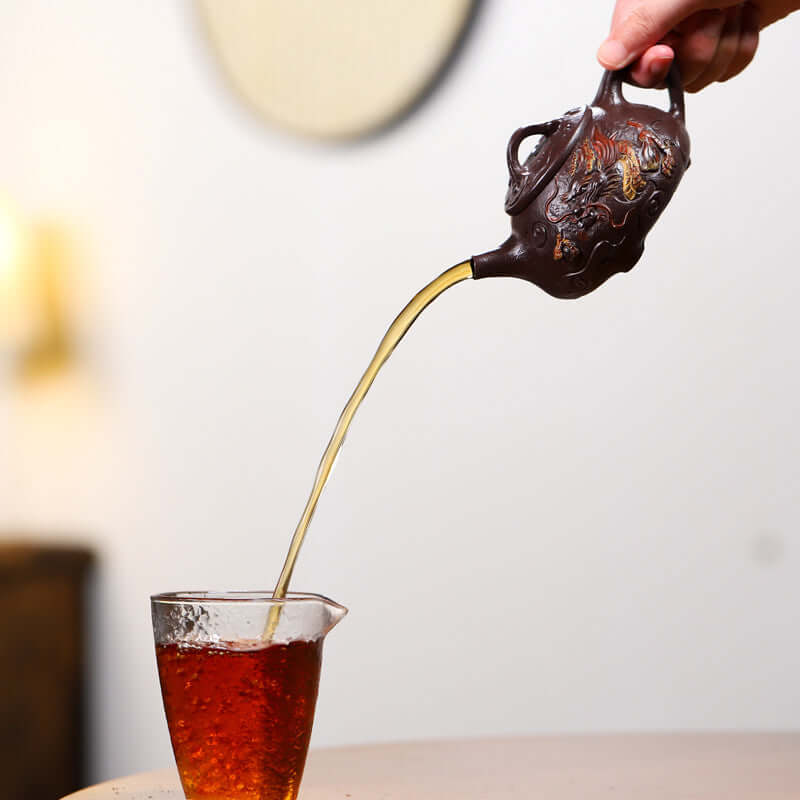 Handmade Yixing purple sand teapot pouring tea into a glass, showcasing traditional craftsmanship and rich color.