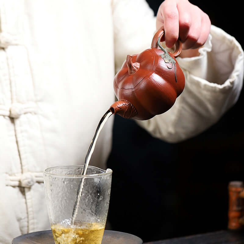 Handmade Yixing purple sand teapot pouring tea into a glass, showcasing craftsmanship and elegant design.