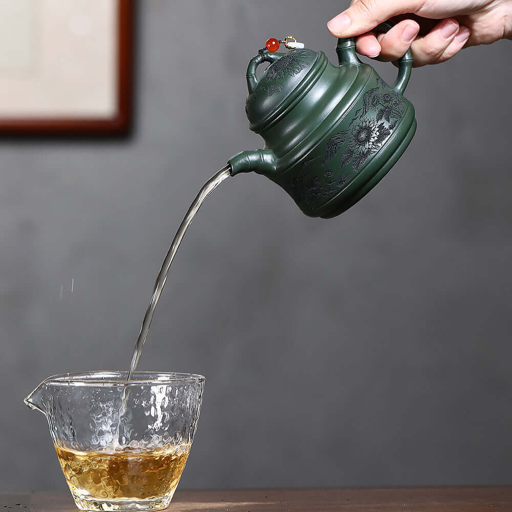 Handmade Yixing purple sand teapot pouring tea into glass cup, engraved with flowers and birds, perfect for Kung Fu tea sets.