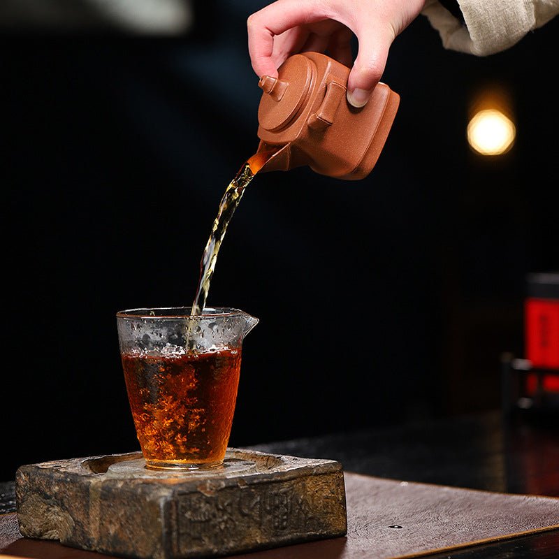 Handmade Yixing purple sand teapot pouring tea into a glass cup, showcasing traditional kung fu tea art.