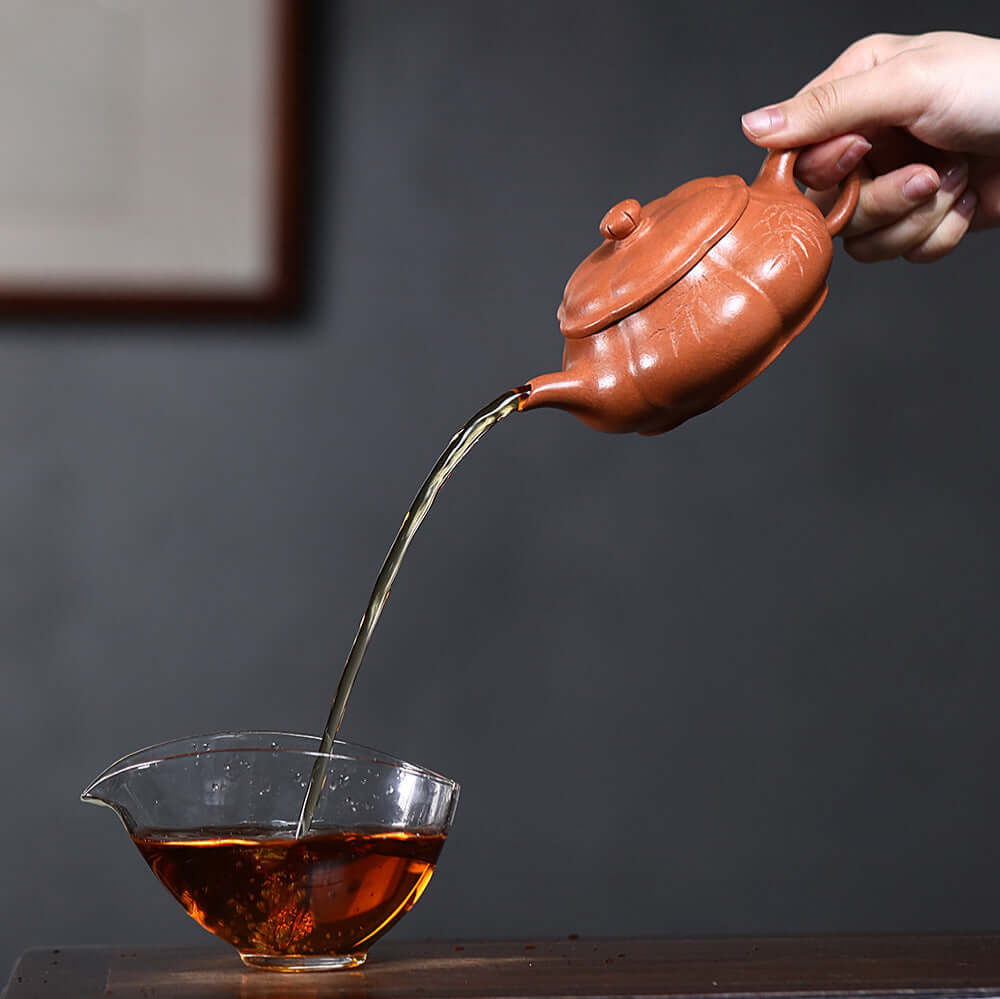 Handmade Yixing purple sand teapot pouring tea into a clear cup, showcasing traditional kung fu tea set.