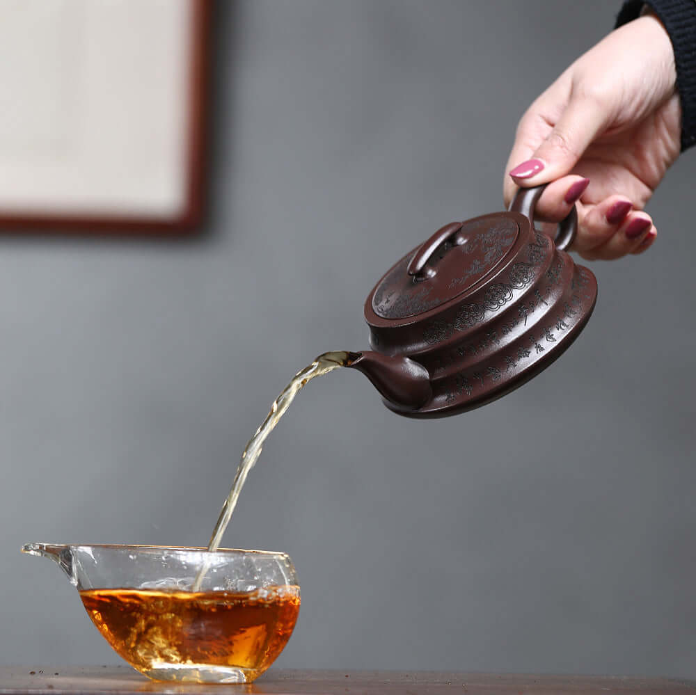 Handmade Yixing purple sand teapot pouring tea into a glass cup, showcasing traditional kung fu tea ceremony.
