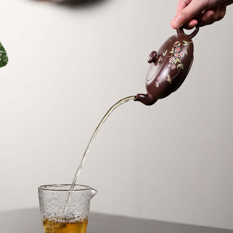 Handmade Yixing purple sand teapot pouring tea into a glass cup, showcasing traditional craftsmanship and elegance.