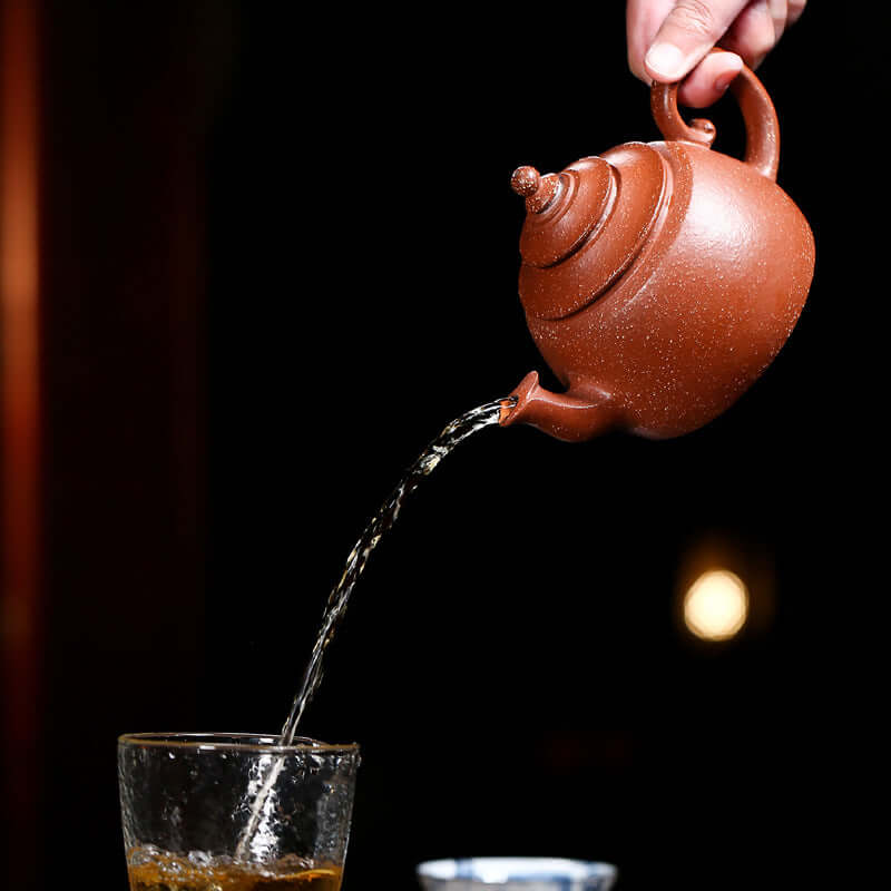 Handmade Yixing purple sand teapot pouring tea into a glass, showcasing traditional Chinese tea culture.