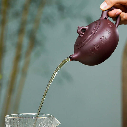 Handmade Yixing purple sand teapot pouring water into a glass, showcasing its elegant design and craftsmanship.