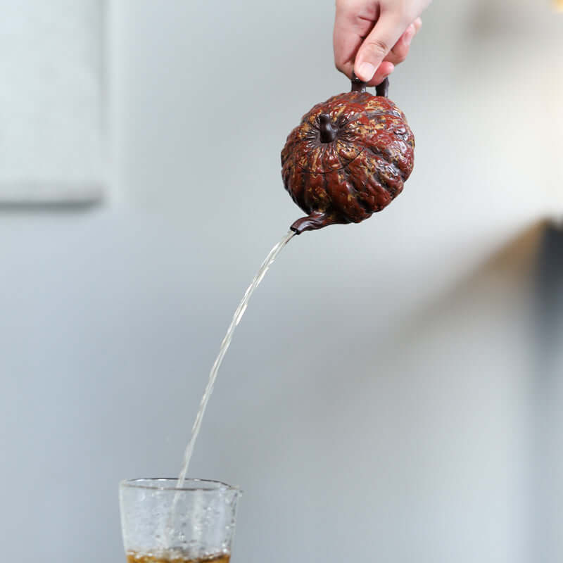 Handmade Yixing purple sand teapot displaying pumpkin shape, pouring tea into a glass.