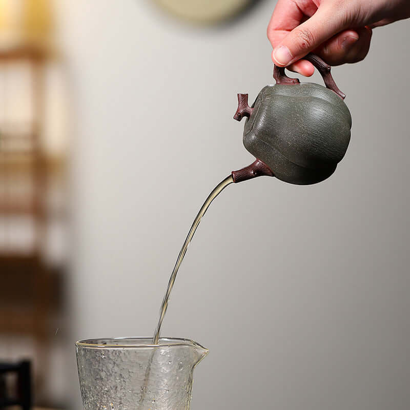 Handmade Yixing purple sand teapot pouring tea into a glass, showcasing elegant craftsmanship and design.