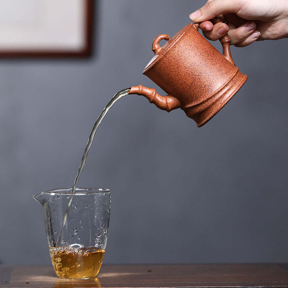 Handmade Yixing purple sand teapot pouring tea into a glass, showcasing traditional Chinese Kung Fu tea set.