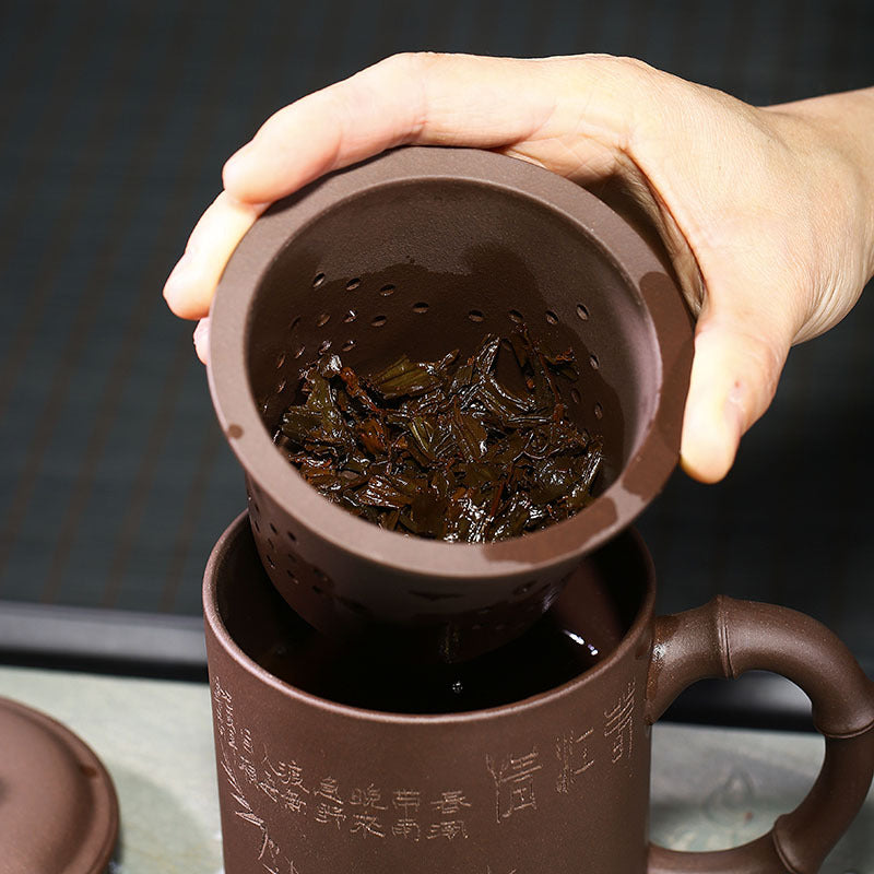 Handmade Yixing purple sand cup featuring a tea strainer with brewed tea leaves, ideal for tea lovers.