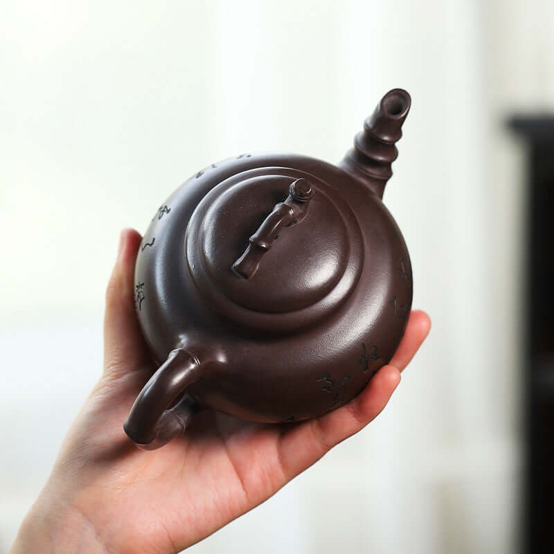 Handmade Yixing purple sand teapot held in hand, showcasing its elegant design and craftsmanship.