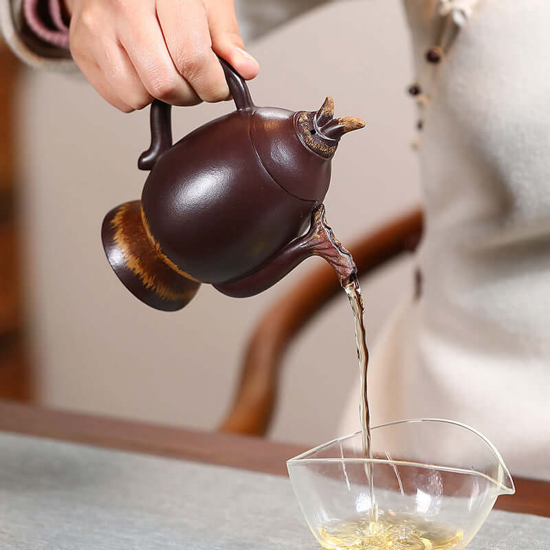 Handmade Yixing purple sand teapot pouring tea into a glass cup, showcasing traditional craftsmanship and elegant design.