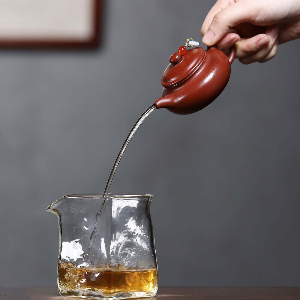 Handmade Yixing purple sand teapot pouring tea into glass carafe, showcasing traditional and elegant tea brewing.