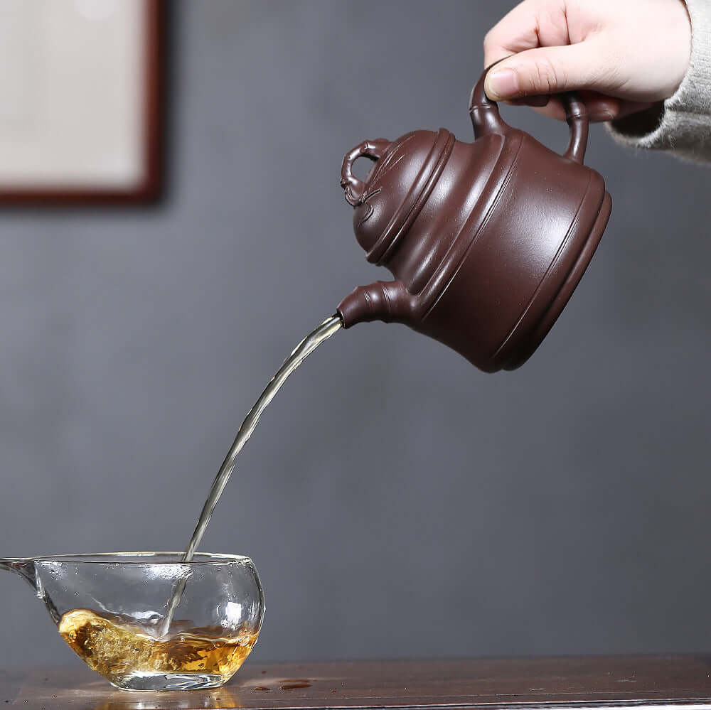 Handmade Yixing purple sand teapot pouring tea into a glass cup, showcasing original craftsmanship for Kung Fu tea.
