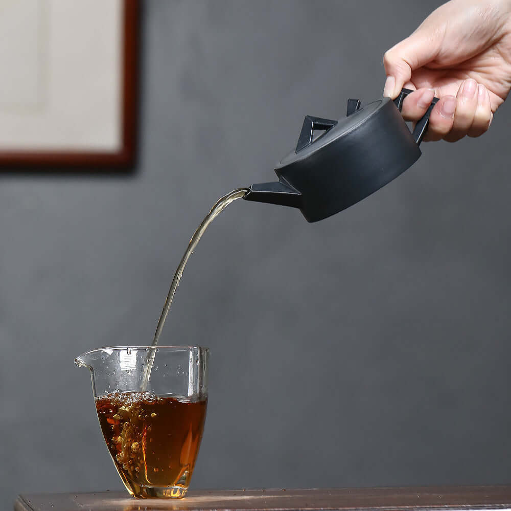 Handmade Yixing purple sand teapot pouring tea into a glass cup, showcasing artisan craftsmanship and traditional tea culture.