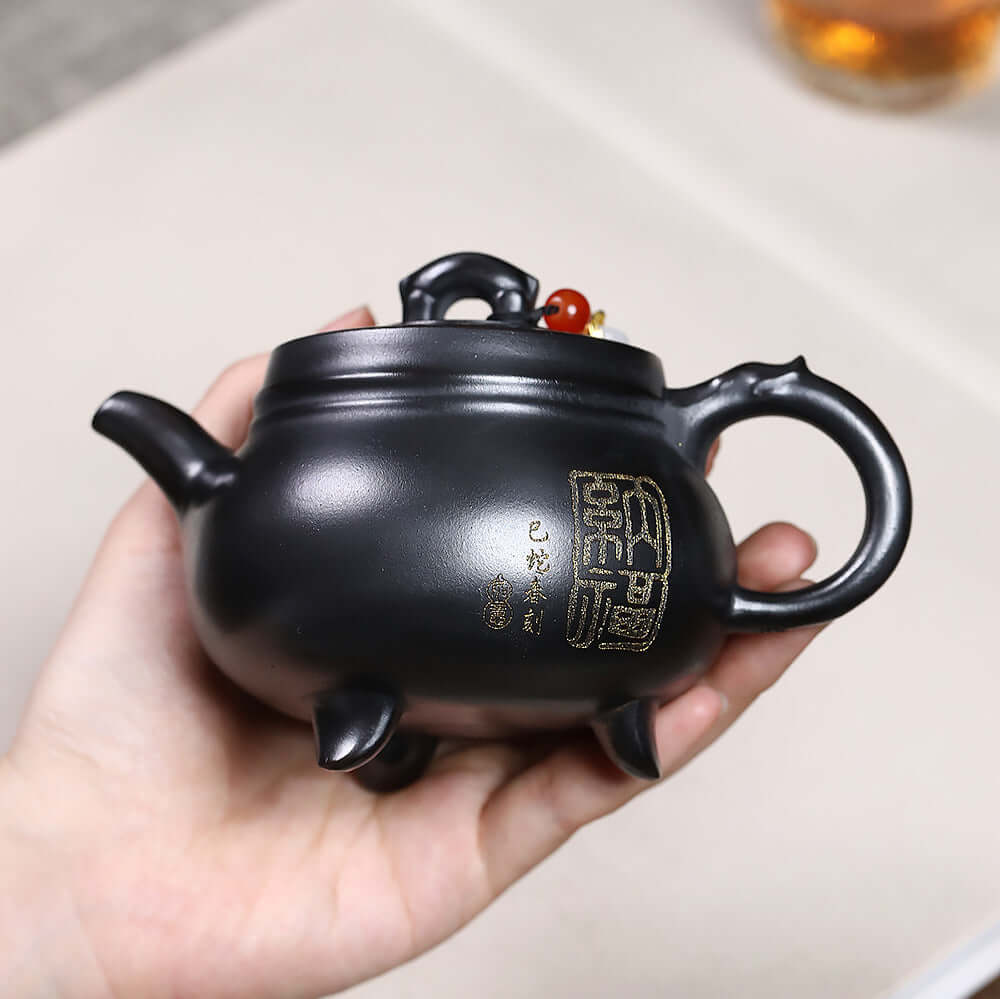 Handmade Yixing purple sand teapot in a hand, featuring a three-legged design, perfect for Kung Fu tea ceremonies.