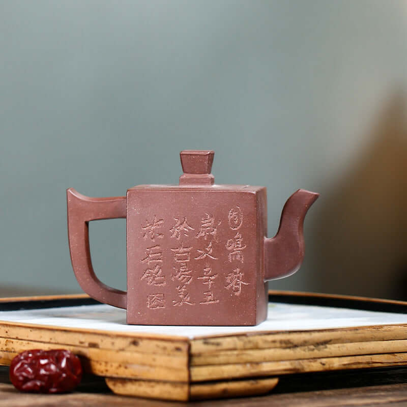 Handmade Yixing purple sand teapot with square design and intricate lettering, showcasing traditional craftsmanship.