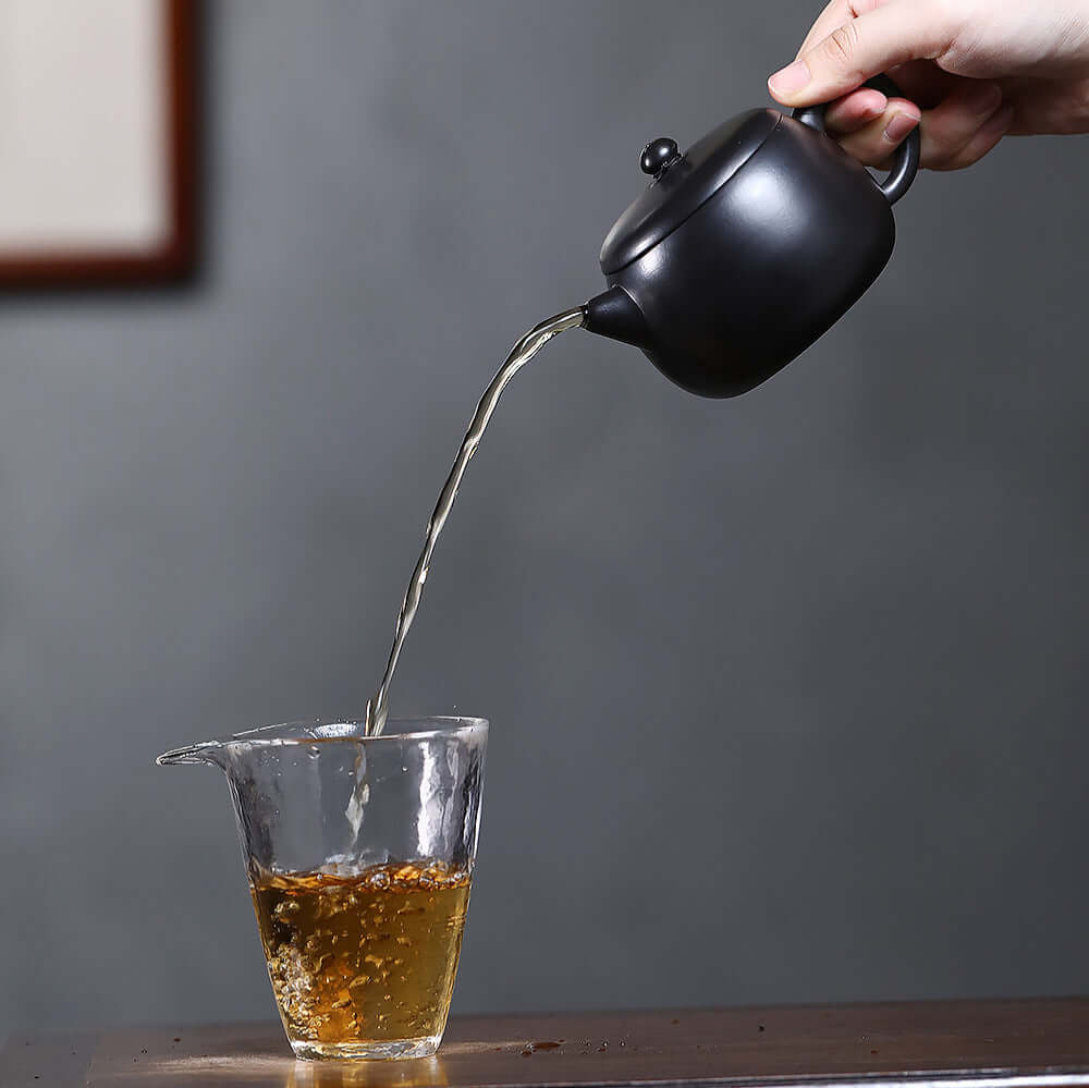 Handmade Yixing purple sand teapot pouring tea into a glass, showcasing traditional Kung Fu tea style.