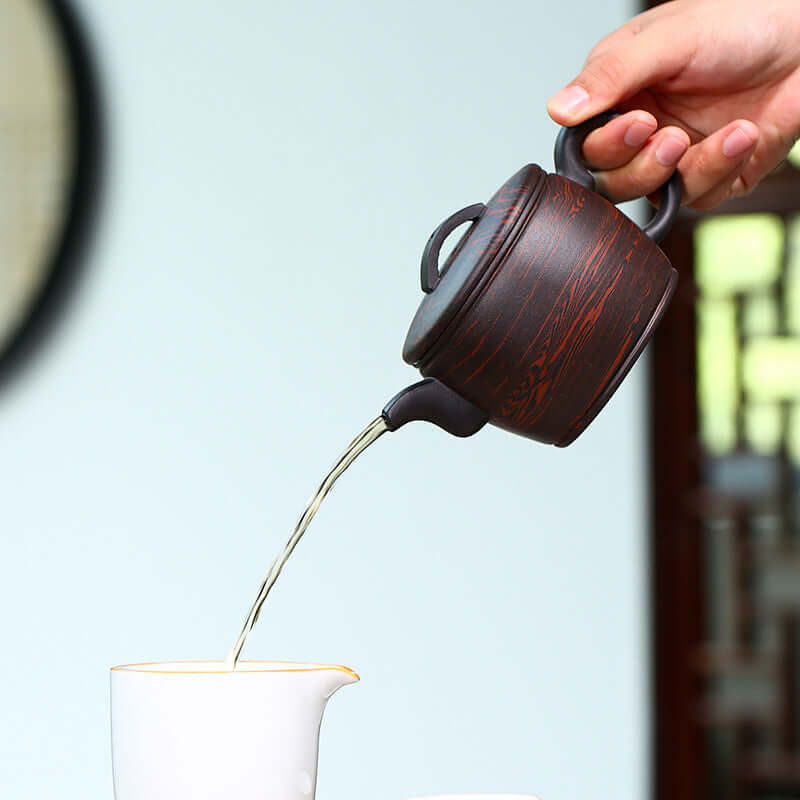 Handmade Yixing purple sand teapot pouring hot tea into a ceramic cup, showcasing exquisite craftsmanship.