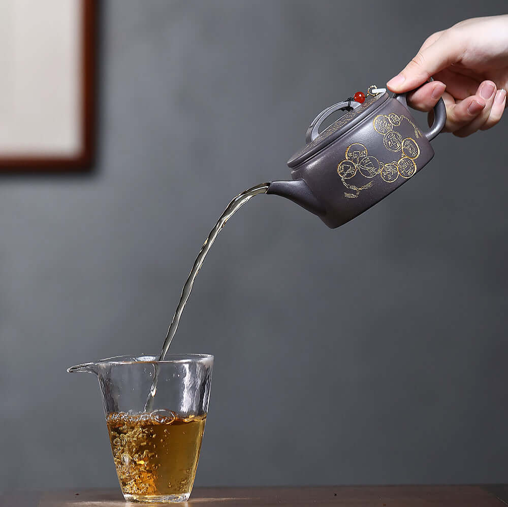 Handmade Yixing purple sand teapot pouring tea into a glass, showcasing elegant craftsmanship and traditional design.