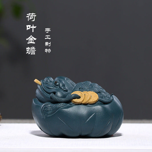 Handmade Yixing purple sand tea pet decoration featuring a golden toad resting on a lotus leaf.
