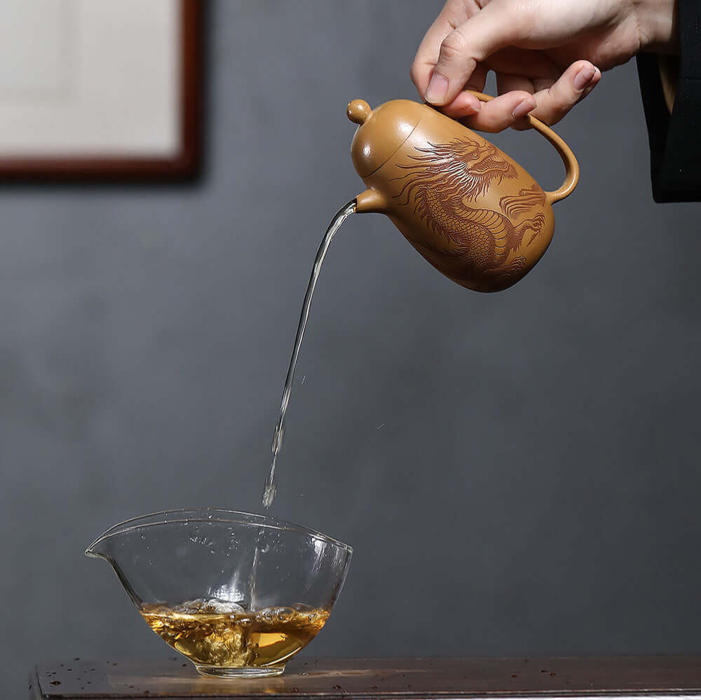 Handmade Yixing purple sand teapot pouring tea into a glass bowl, showcasing traditional kung fu tea craftsmanship.