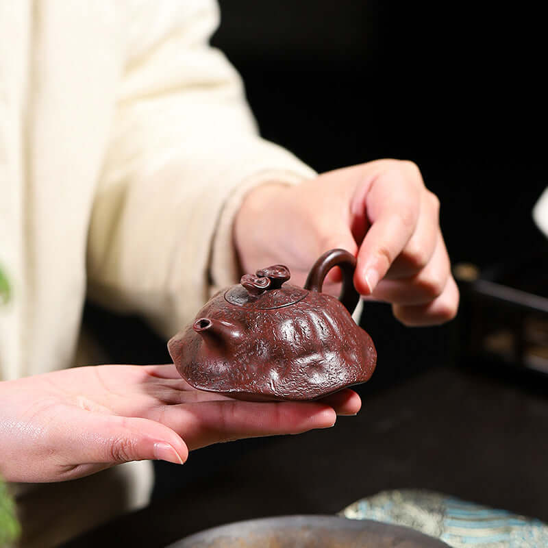 Handmade Yixing purple sand teapot held in hand, showcasing its unique design and rich iron red color.