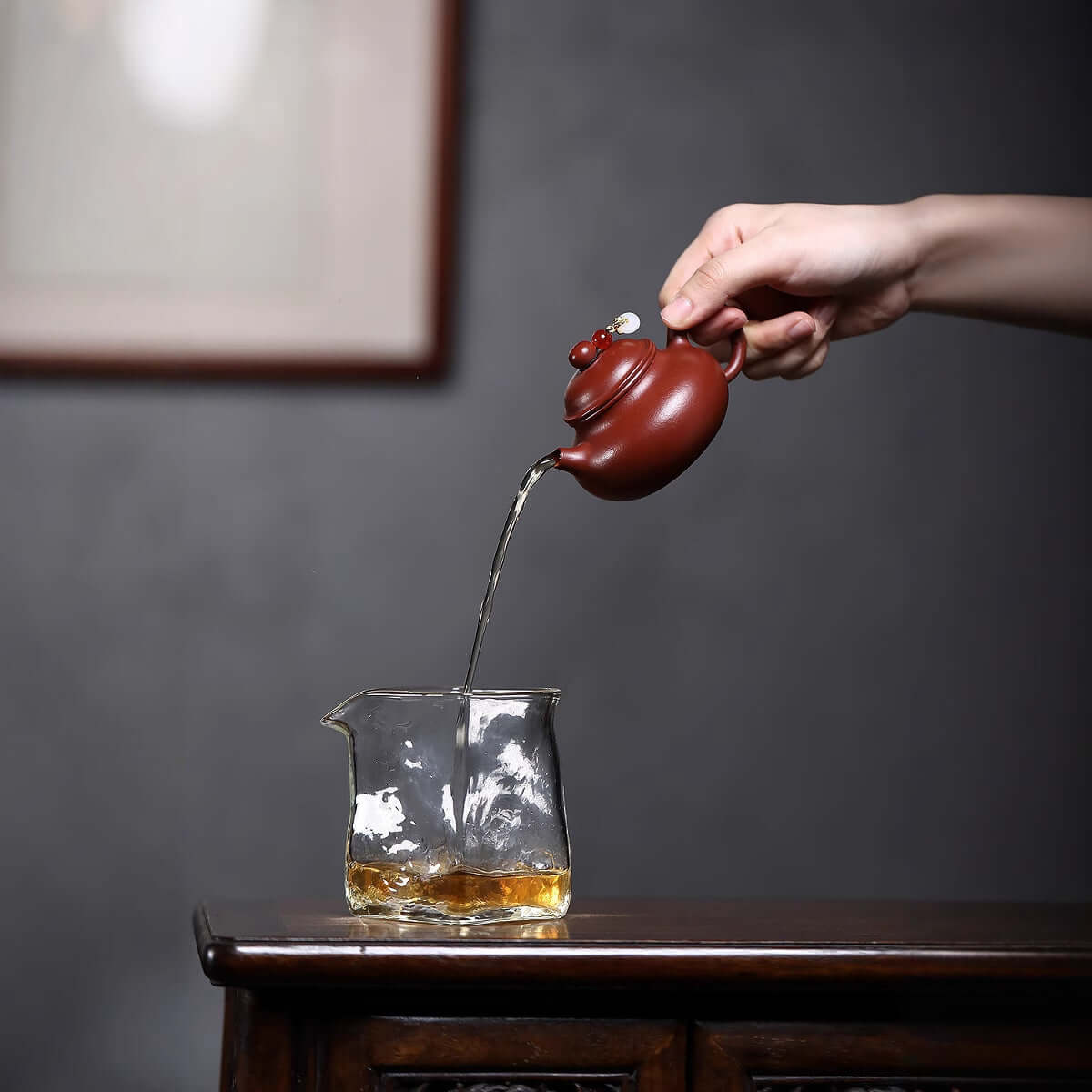 Handmade Yixing purple sand teapot pouring tea into a glass pot, showcasing original craftsmanship in a classy setting.