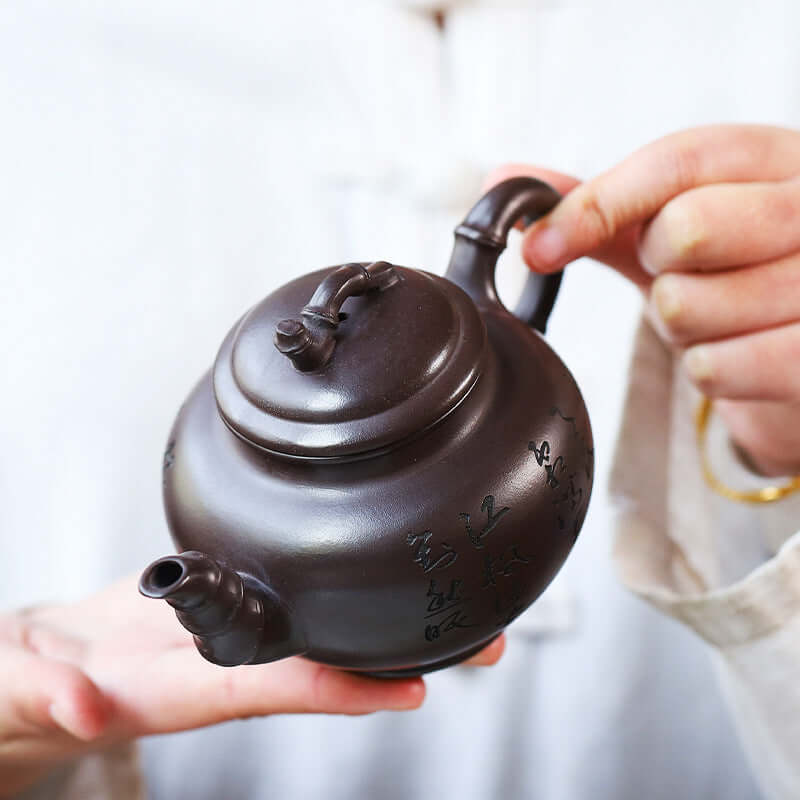 Handmade Yixing purple sand teapot held by a person, showcasing elegant design and craftsmanship.