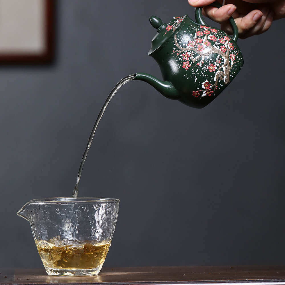 Handmade Yixing purple sand teapot pouring tea into glass cup, showcasing original craftsmanship and elegance.
