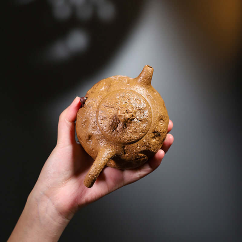 Handmade Yixing purple sand teapot held in hand, showcasing unique texture and design.