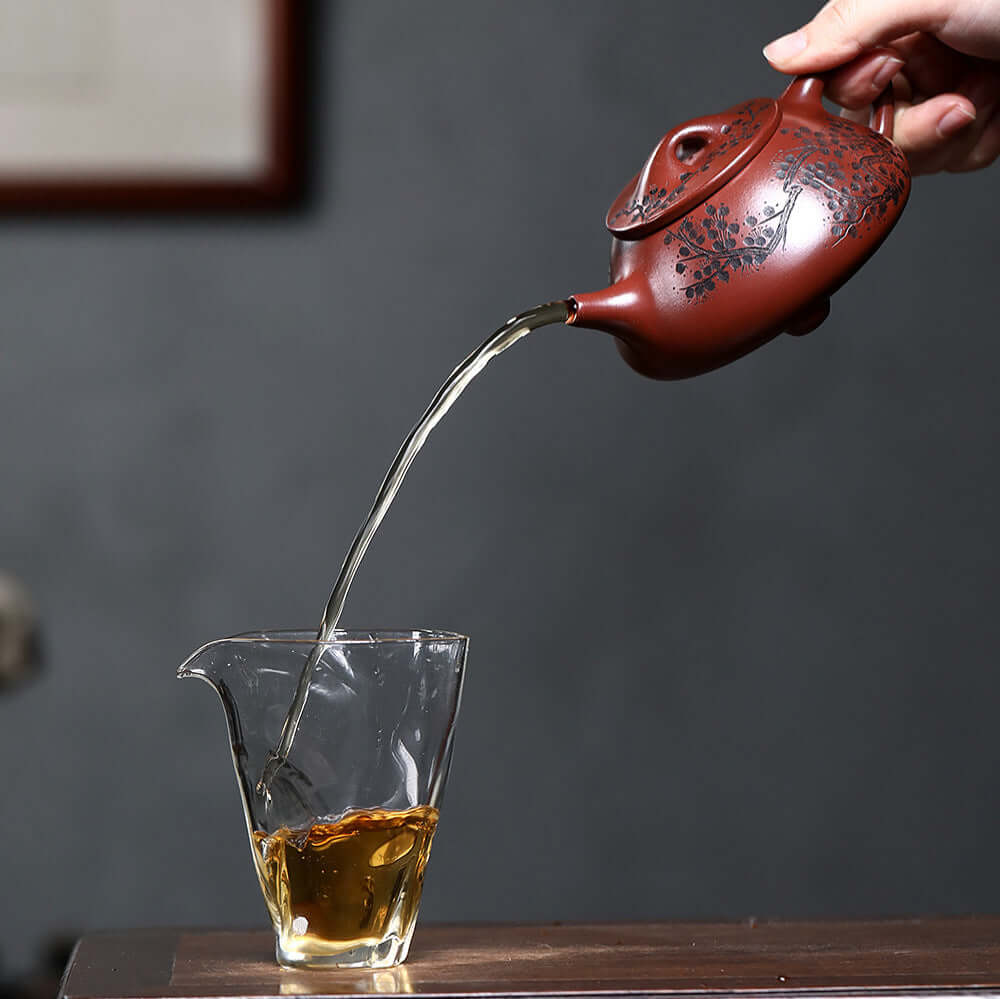 Handmade Yixing purple sand teapot pouring tea into a glass cup, showcasing traditional kung fu tea ceremony.