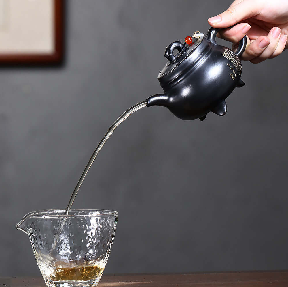 Handmade Yixing purple sand teapot pouring tea into glass cup, showcasing traditional Kung Fu tea set art.