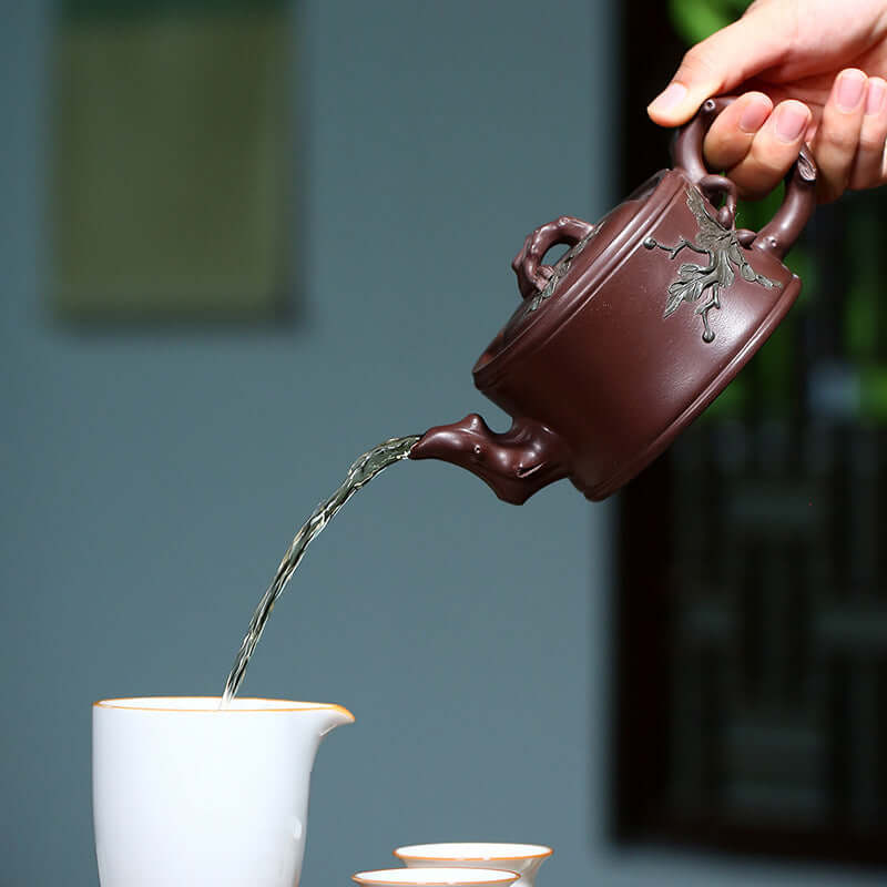 Handmade Yixing purple sand teapot pouring water into a cup, showcasing traditional craftsmanship and elegant design.