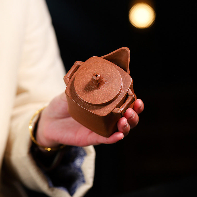 Handmade Yixing purple sand teapot, four-square design, held by a hand, perfect for traditional kung fu tea ceremonies.